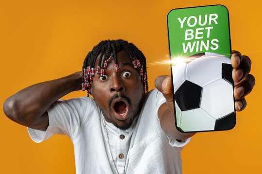 Man celebrates winning sports bet while holding phone with soccer ball on bright background