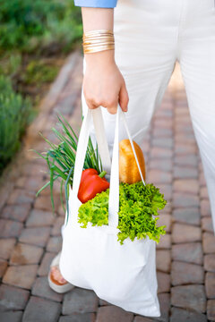 Woman holds white canvas tote bag with fresh vegetables in park. Zero waste sustainable eco concept.