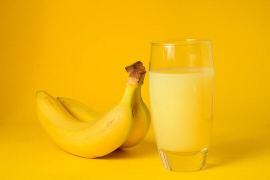 Vaso de zumo de platano natural acompa&ntilde;ado de platanos frescos sobre un fondo amarillo. Concepto de alimentaci&oacute;n saludable, bebida refrescante, fruta de verano y fotograf&iacute;a de producto en estudio 