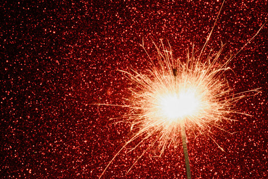 Festive sparkler light with glowing sparks on red glitter background. Elegant holiday celebration concept ideal for New Year design, greeting cards, banners, marketing materials and promotions