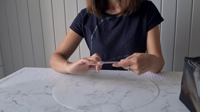 A woman is doing her manicure using a nail file.