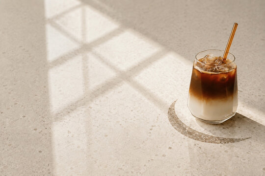 Layered iced coffee with milk and glass straw in warm sunlight