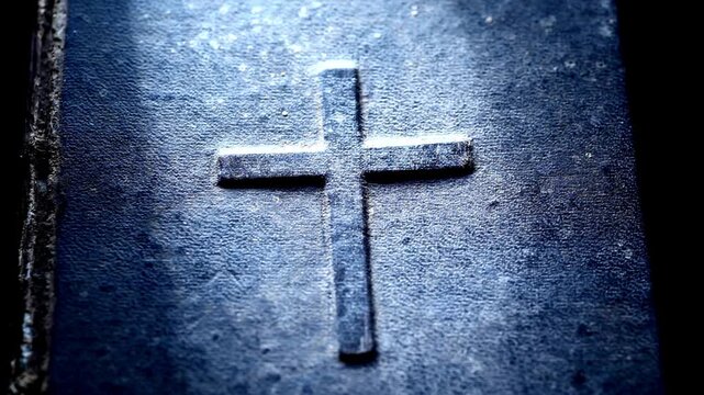 A weathered bible with an embossed cross illuminated by gentle sunlight highlighting textured book cover.