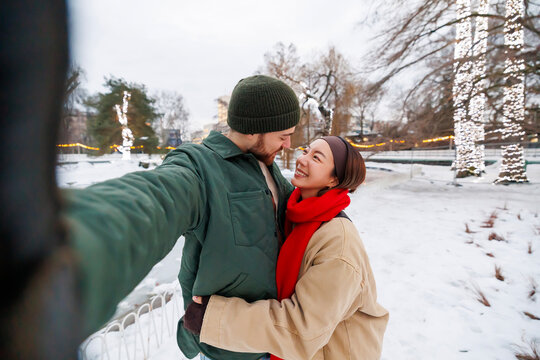 Couple having fun taking selfies while walking in the park on snowy winter day