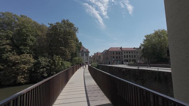 Walking POV crossing the modern wooden pedestrian bridge beside the Smedenpoort into the historic center of Bruges, Belgium