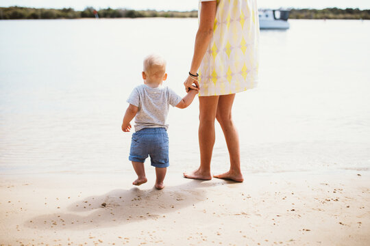 Rear view of a barefoot Mother and son standing at the water's edge on a sandy beach, Queensland, Australia
