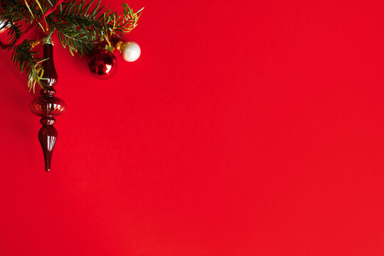 Christmas flat lay. Top left corner border of vintage glass finial ornament, shiny baubles, and fir branch on red background with copy space. Xmas background