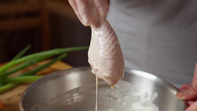 Hand dips raw chicken drumstick into seasoned wet batter for crispy fried chicken
