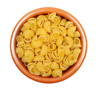 Dry yellow pipe rigate pasta with ribbed, curved shapes pile in clay pot isolated on white background, top view, clipping path