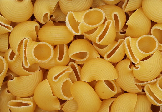 Dry yellow pipe rigate pasta with ribbed, curved shapes pile backgroundand texture, pattern, top view