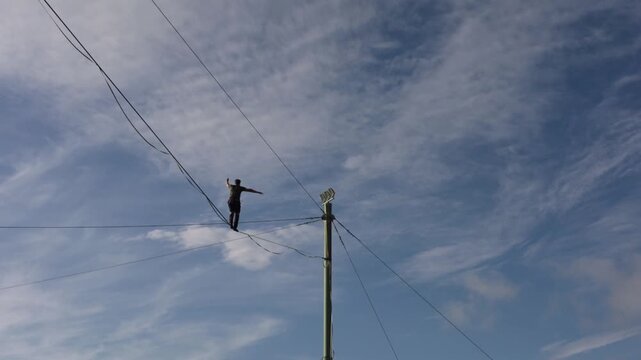 A highwire performer balances on an elevated cable above a river and city, daring outdoor adventure and freedom.
