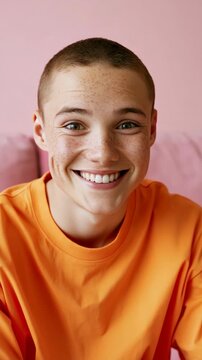 Teen with buzz cut and freckles wearing bright orange shirt against pink background for editorial portrait and youth lifestyle use