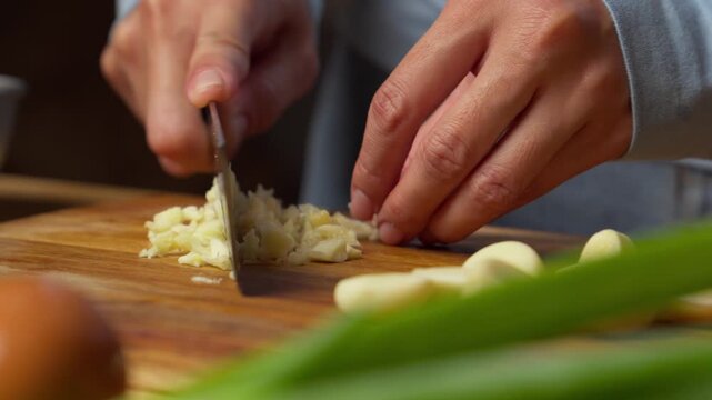 Close-up of hands mincing garlic on wooden board