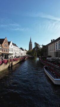 Static vertical shot from a bridge over a Bruges canal with the Church of Our Lady tower in the distance, Belgium