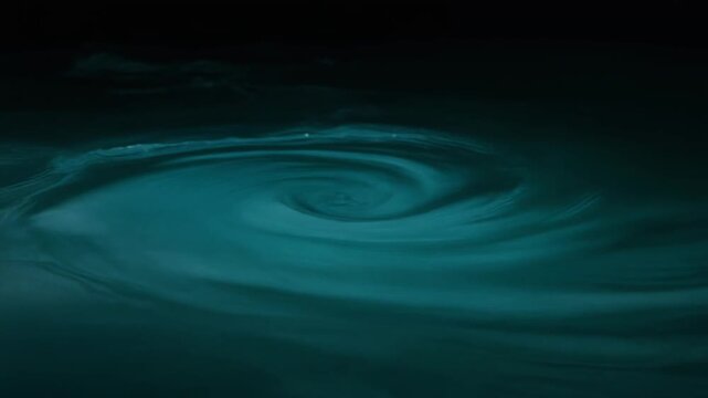 Dark teal-blue water swirls in continuous gentle currents, soft light revealing moving surface texture and subtle depth against near-black background with tranquil natural atmosphere.