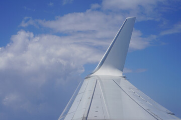 Clear sky with scattered clouds. White airplane tail rises above. Smooth curves of wing and fin. Calm flight high above ground. Ideal for travel or aviation themes © polack
