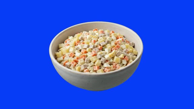 A deep ceramic bowl filled with traditional diced Olivier potato salad isolated against a solid blue background. Suitable for holiday meal promotions, culinary videos, and restaurant menu displays.