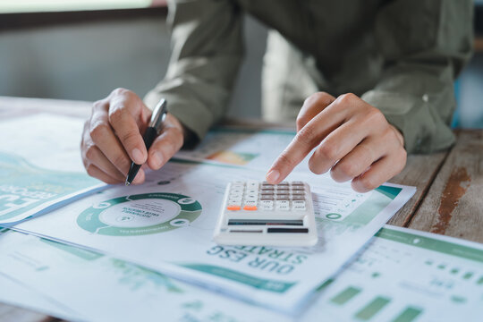ESG investment sustainable finance concept, professional hands using calculator and pen for environmental performance metrics and carbon footprint corporate responsibility report analysis.
