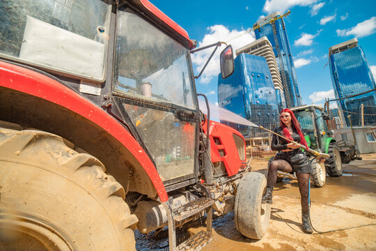 Red haired woman washing tractor on construction site with sky copy space