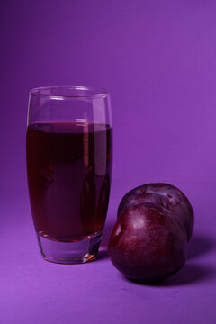 Vaso de zumo de ciruela natural acompa&ntilde;ado de ciruelas frescas sobre un fondo morado. Concepto de alimentaci&oacute;n saludable, bebida natural, fruta fresca y fotograf&iacute;a de producto en estudio.