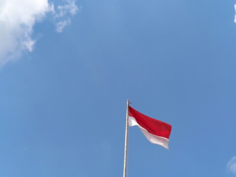 Indonesian red and white flag fluttering naturally in the wind, showcasing the nation's distinctive national colors and symbol of unity. This dynamic patriotic image can be used for Indonesia Independ