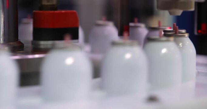 Automated equipment carries blank spray bottles by conveyor belt closeup. Modern robotized production line transports aerosol flasks to fill at factory