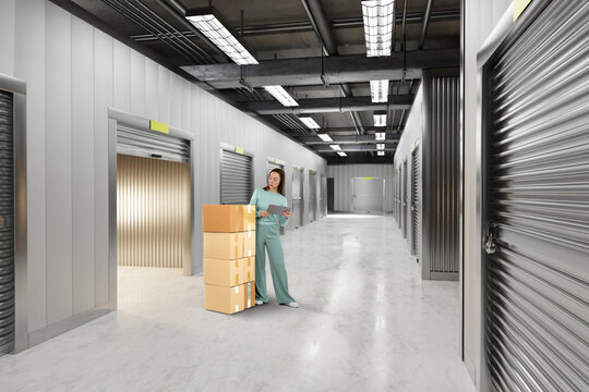 Self storage facility. Woman checks inventory documents beside stacked boxes in a secure storage unit corridor with individual rental rooms.