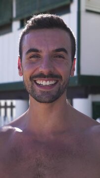 Vertical portrait of a handsome caucasian man at the beach looking at camera smiling while enjoying the summer vacations outdoors.