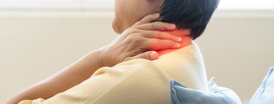 Senior Asian woman suffering from acute neck pain and shoulder stiffness holding her neck with painful expression at home for healthcare concept.