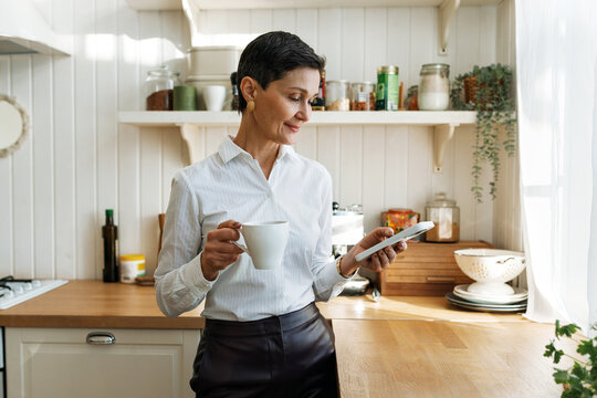Side view of successful elegant classy female entrepreneur checking her smartphone working chat after returning home from work or taking coffee for breakfast before leaving to office
