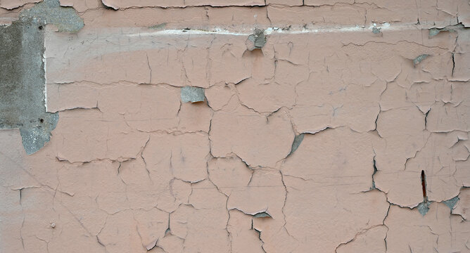 Horizontal view of weatherworn tan paint wall surface with deteriorating cracked peeling paint, exposed rectangular concrete spot, scratch marks, and white paint streaks