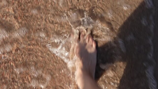 Slow motion of walking along the sandy shoreline of Lake Issyk-Kul with bare feet in the water, Kyrgyzstan, 4K video