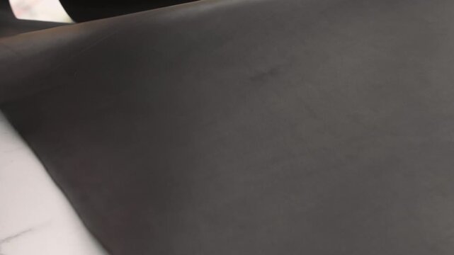 Leatherworker rolling out a piece of black natural leather on a marble workshop table for crafting