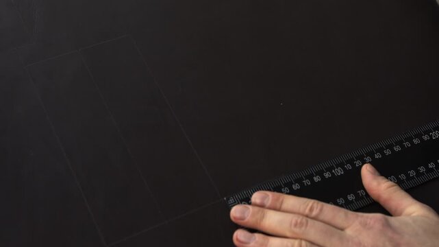Leather craftsman marking lines with ruler and awl for cutting leather material in a workshop, creating a pattern for a handmade product