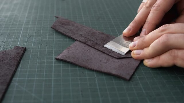 Craftsman skiving and thinning leather edges with a sharp knife on a cutting mat in a traditional workshop