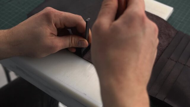 Leatherworker making holes in a brown leather wallet using a hammer and a punch tool in a workshop
