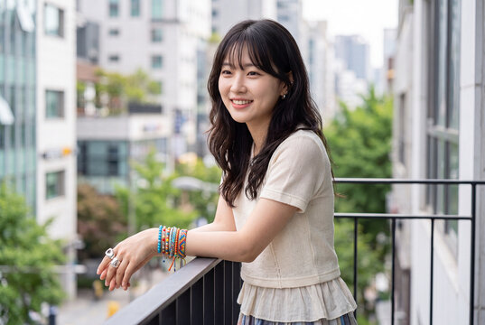 Portrait of a smiling korean woman on a balcony in casual summer outfit for lifestyle banner and social media background