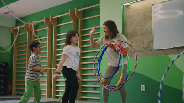 Kids are actively exercising with hula hoops in a bright, energetic gym setting. Children are seen having fun and engaging in playful activity during a physical education class.