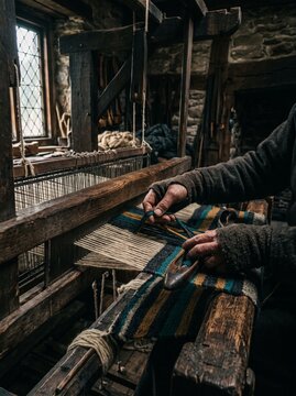 Close up of skilled artisan hands operating a vintage wooden loom to weave colorful yarn, traditional textile craft, authentic handmade lifestyle.