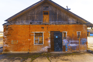 Weathered brick warehouse facade with boarded gable, barred window, and worn metal entrance door © ossyffer