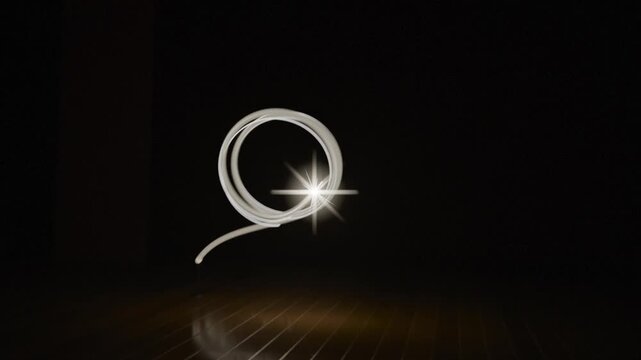 Appearing bright point of light drawing looping rings across dark studio, reflecting on wood floor