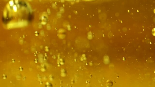 Golden oil bubbles float through an amber liquid in a glowing macro. Concept food branding, cosmetic packaging, banners, websites and abstract advertising.