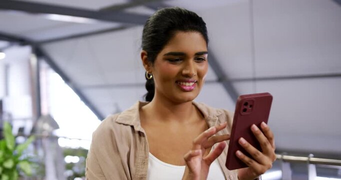 Adult Indian woman reading message at office in beige top holding maroon phone, tapping, checking