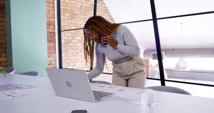 Woman taking phone call while leaning over table, using laptop and reviewing charts for work