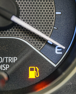 Macro close-up of a car dashboard fuel gauge needle pointing to empty (E), with a fuel pump warning icon illuminated, Low Fuel Warning Light on car Dashboard Display