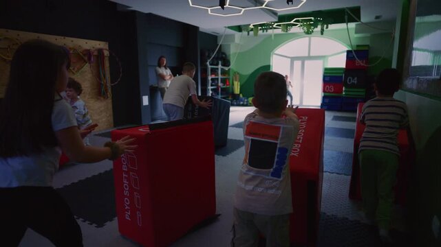 Children actively engage in physical training, pushing colorful soft plyo boxes across a gym floor. Young kids enjoy a dynamic exercise session, developing strength and coordination.