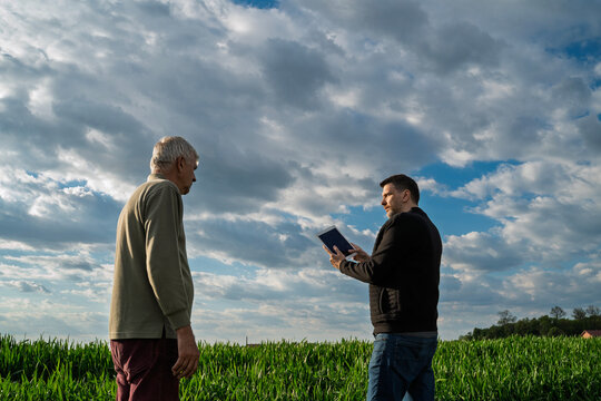 Agriculture expert with tablet standing on a field and talking to a farmer , clouds and copy space