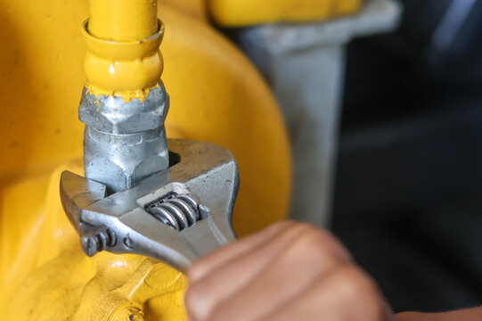 Worker using an adjustable wrench on a yellow industrial pipe.