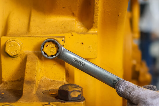 Mechanic using a ring spanner on a yellow machine bolt.