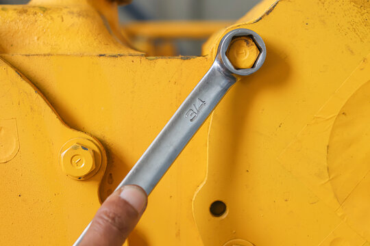 Wrench tightening a bolt on yellow industrial machinery.